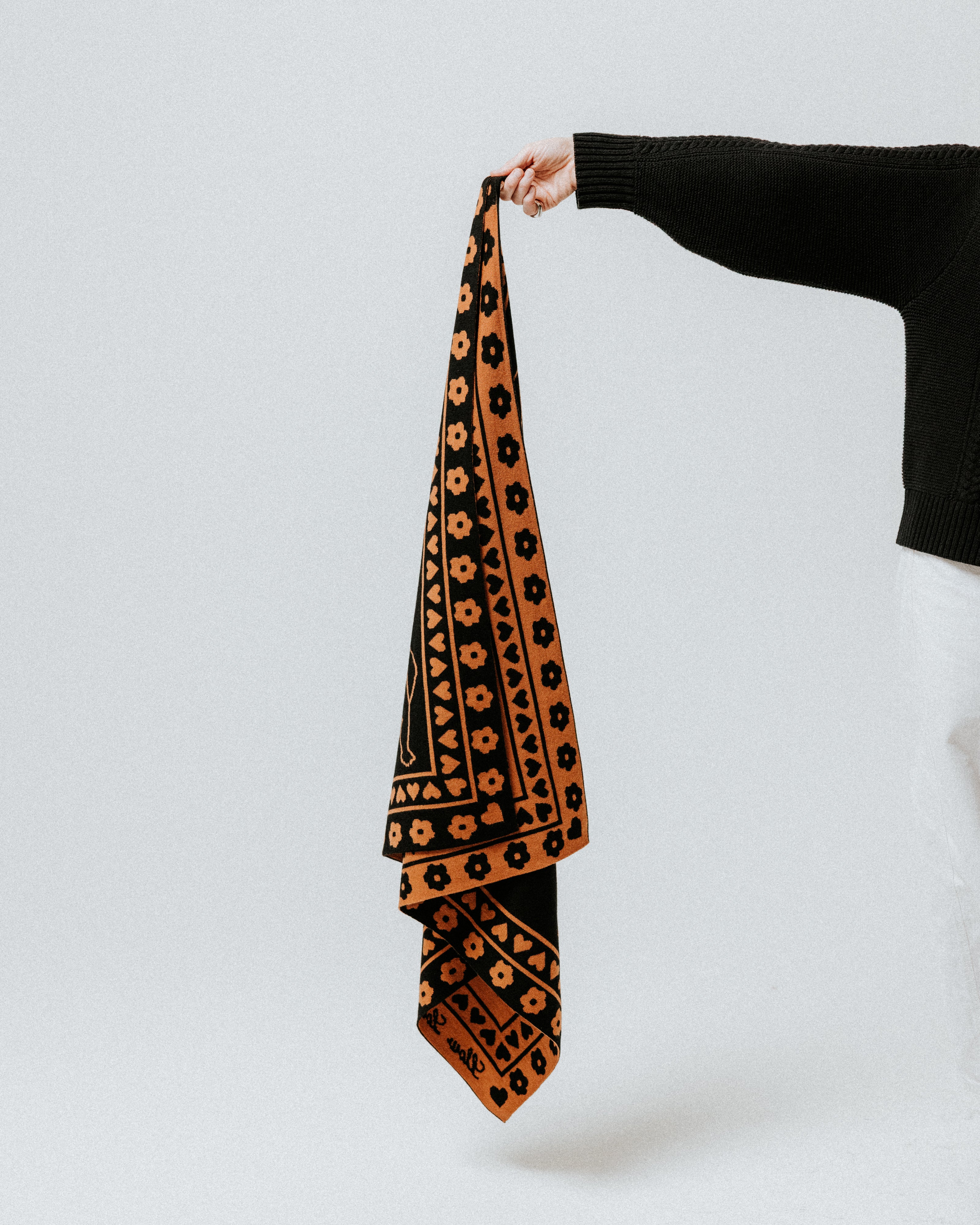 The Slow Love luxury merino wool bandana scarf in toffee and black, a warm knitted accessory featuring the signature Cherub design.