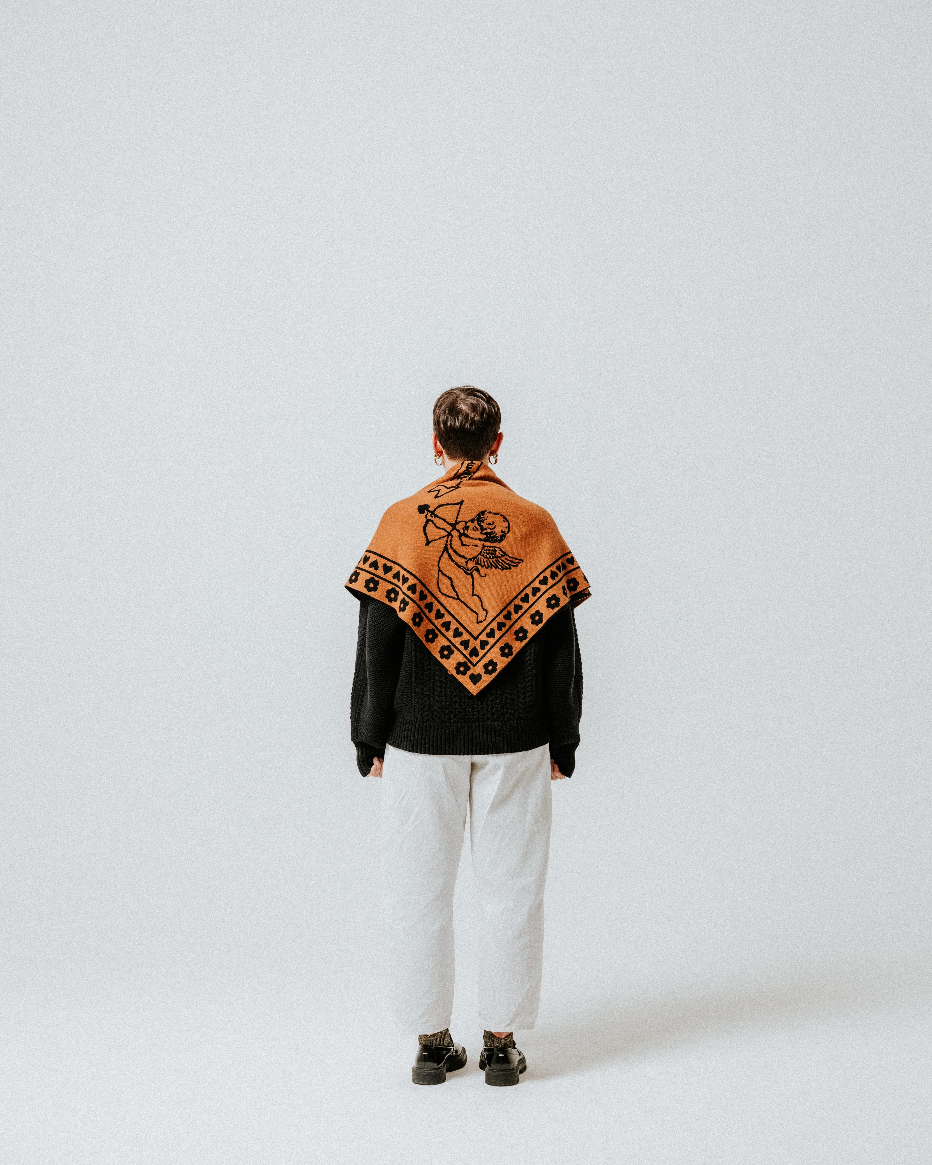 The Slow Love Cherub Scarf in toffee and black, knitted from 100% merino wool with a distinctive cherub design.