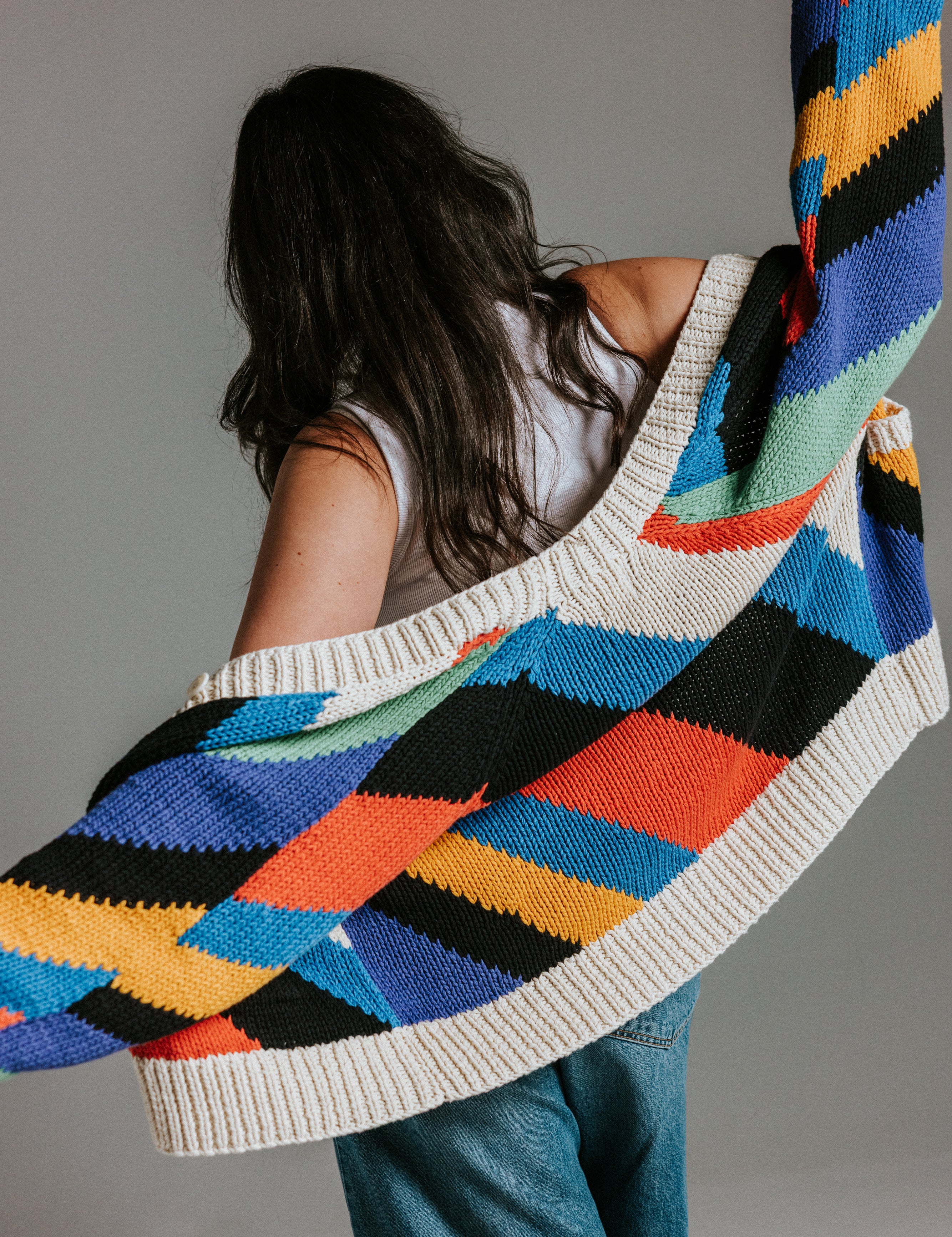 Model wearing oversized handknit cotton cardigan with seven colour intarsia stripe pattern by Slow Love Knitwear