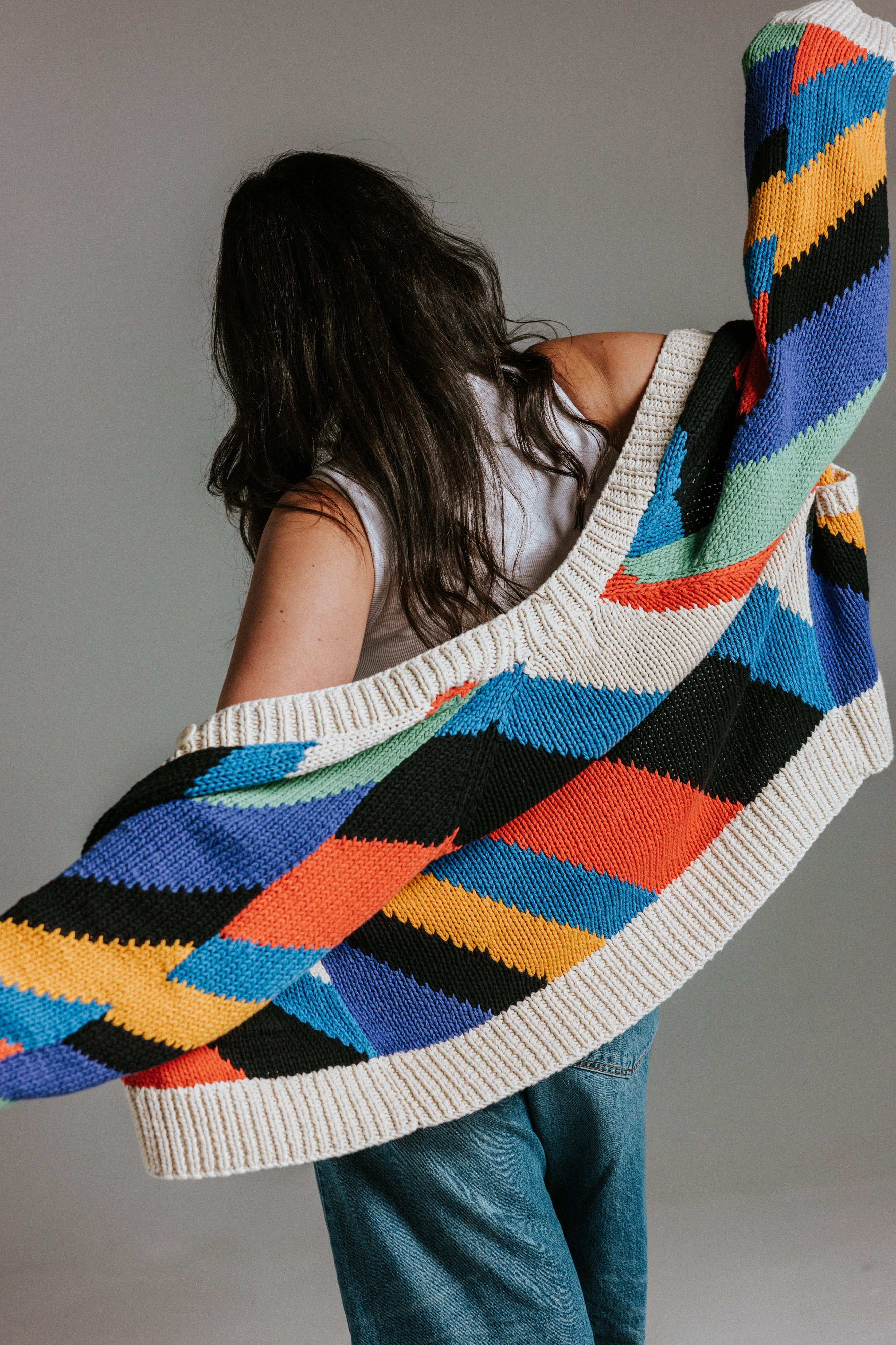 Model wearing oversized handknit cotton cardigan with seven colour intarsia stripe pattern by Slow Love Knitwear