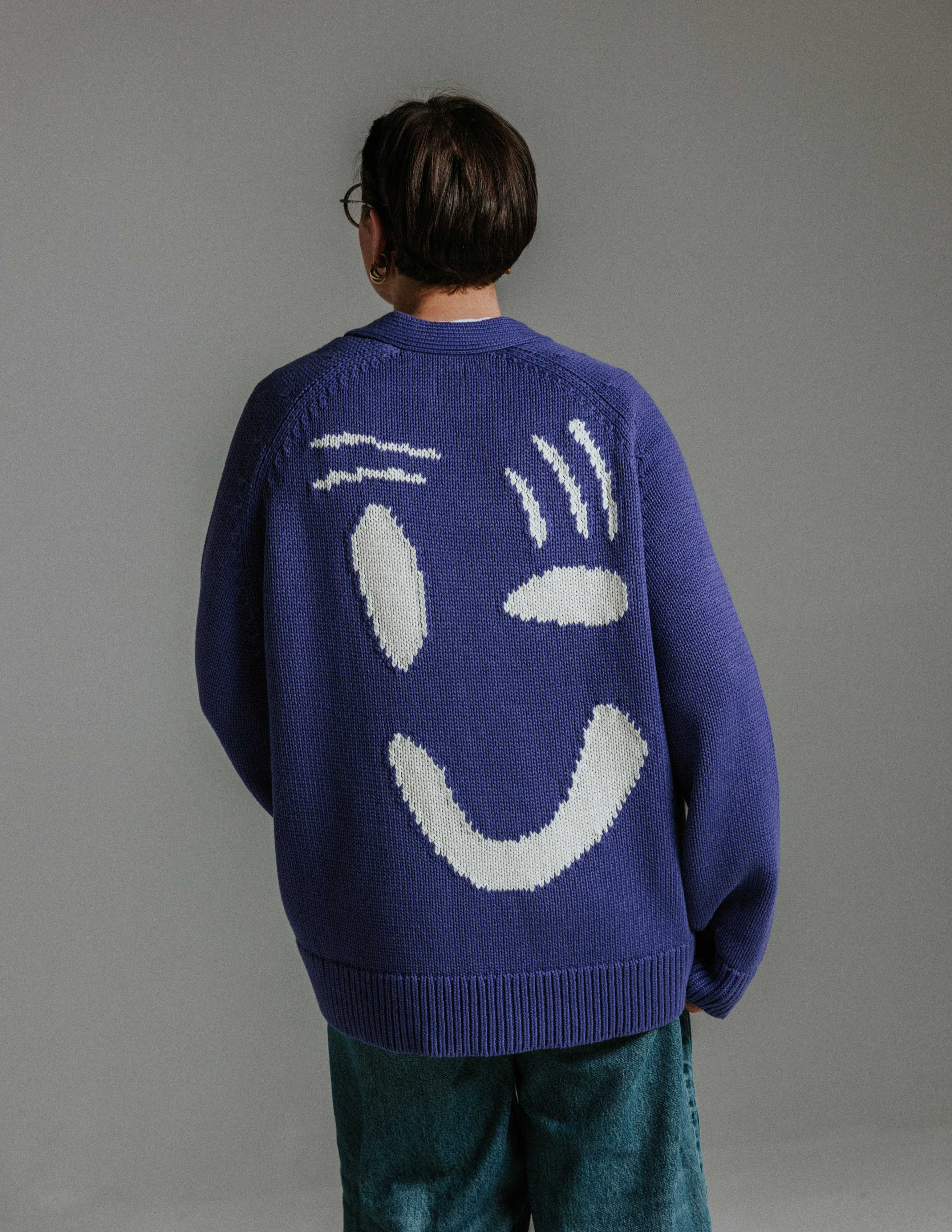 Back of oversized faded indigo and white cotton cardigan by Slow Love Knitwear with large smiley face design