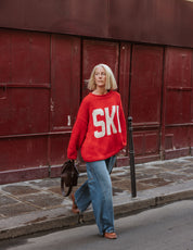 Off-white ski motif across the front of The Slow Love Ski Season Hand Knit Jumper, set against a bold red 100% cotton knit.